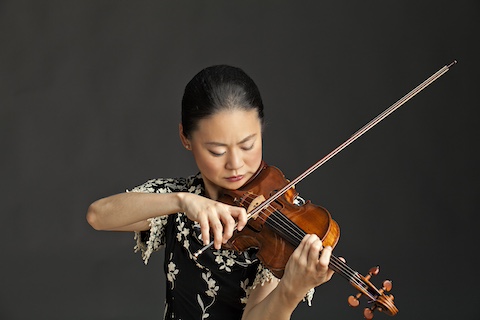 Japanese woman playing violin against dark background