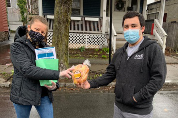 a woman wearing a cloth face mask hands a challah to a man wearing a surgical mask