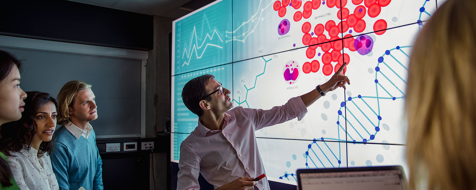 Teacher and students looking at a brightly colored scientific slide projected on a screen in a darkened room