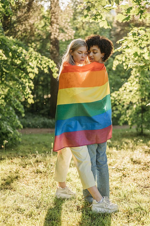 two hugging women wrapped in an LGBT flag
