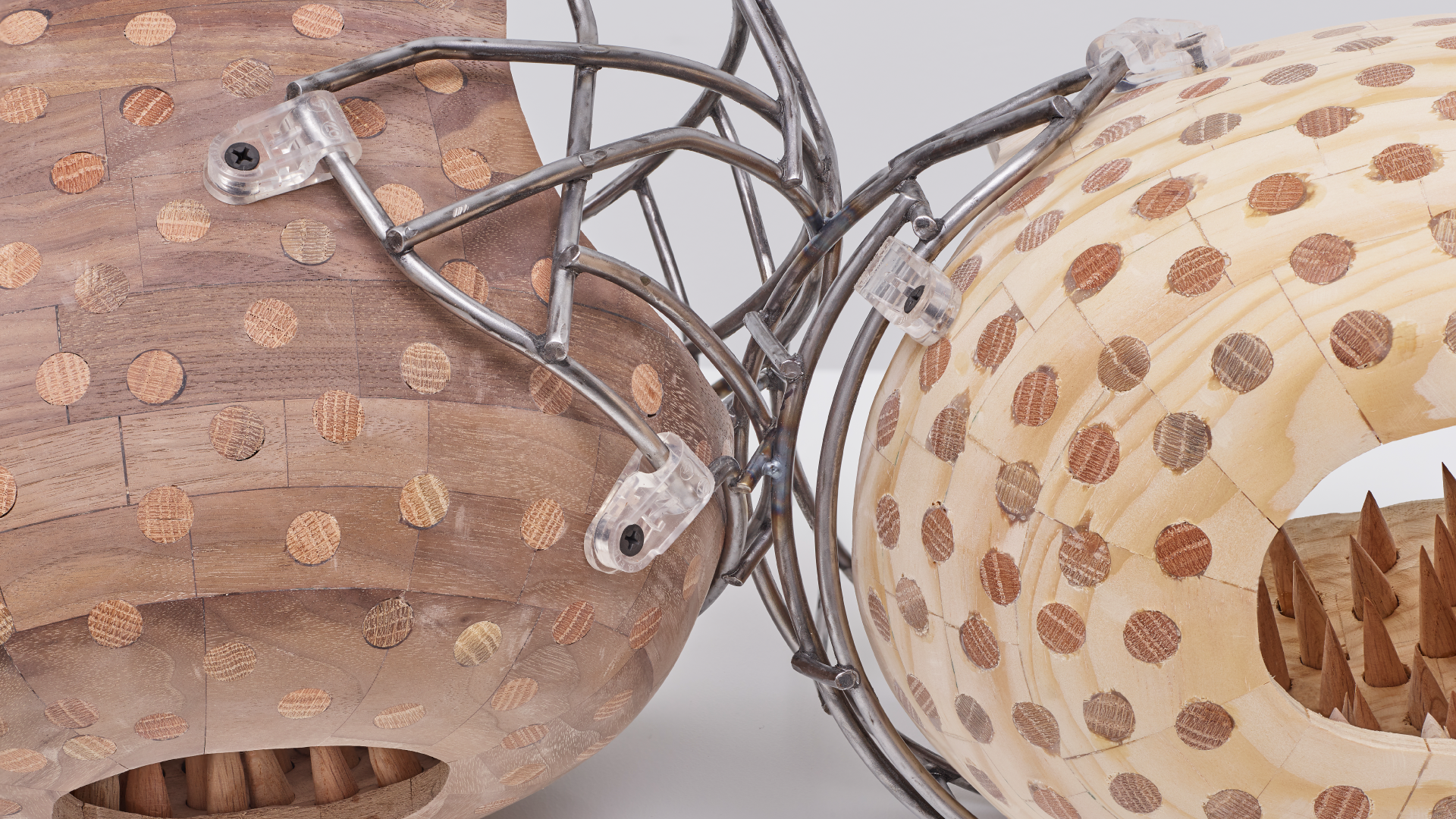 Two wooden football helmets linked together to look like they are kissing with wooden spikes on the interior.