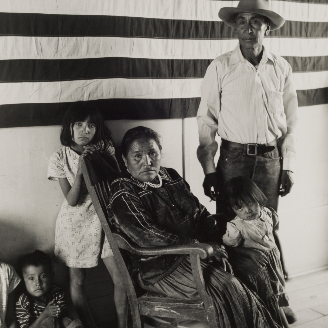 Black and white portrait of a Native American family against an American flag.