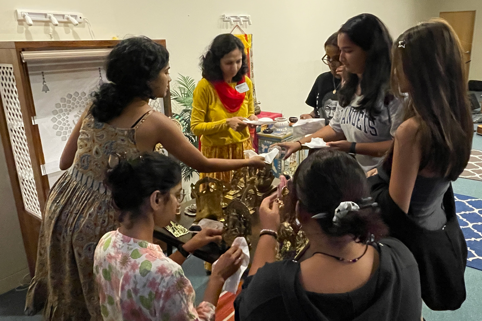 group of women who appear Indian gathered around a table cleaning objects, with an altar in the background