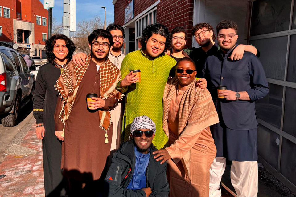 a group of 9 young men standing on a street with clothes that look Muslim with arms around each other smiling into the camera