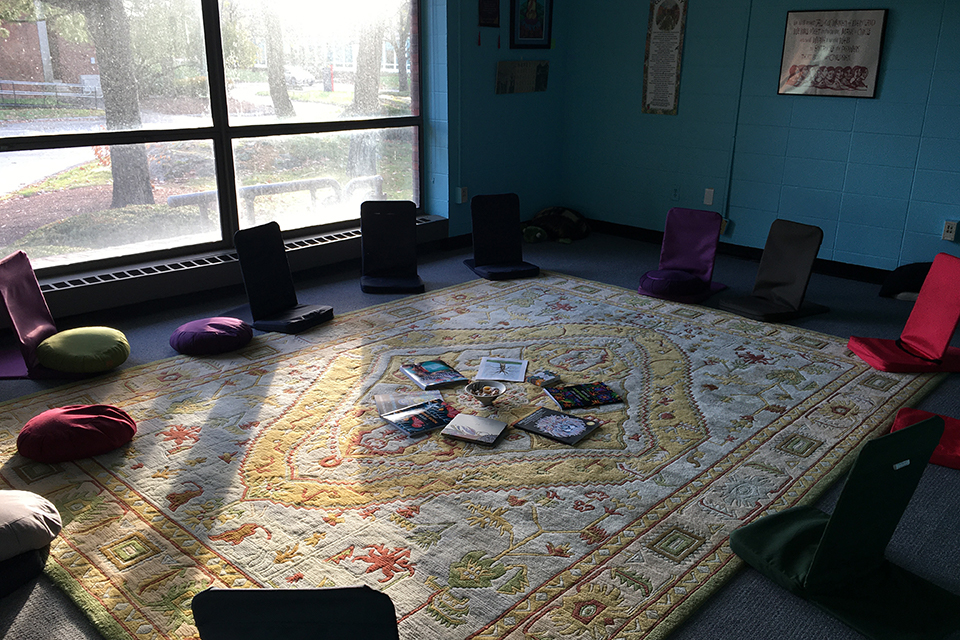 picture of backjacks and meditation cushions in a circle on a rug with a large window in the background