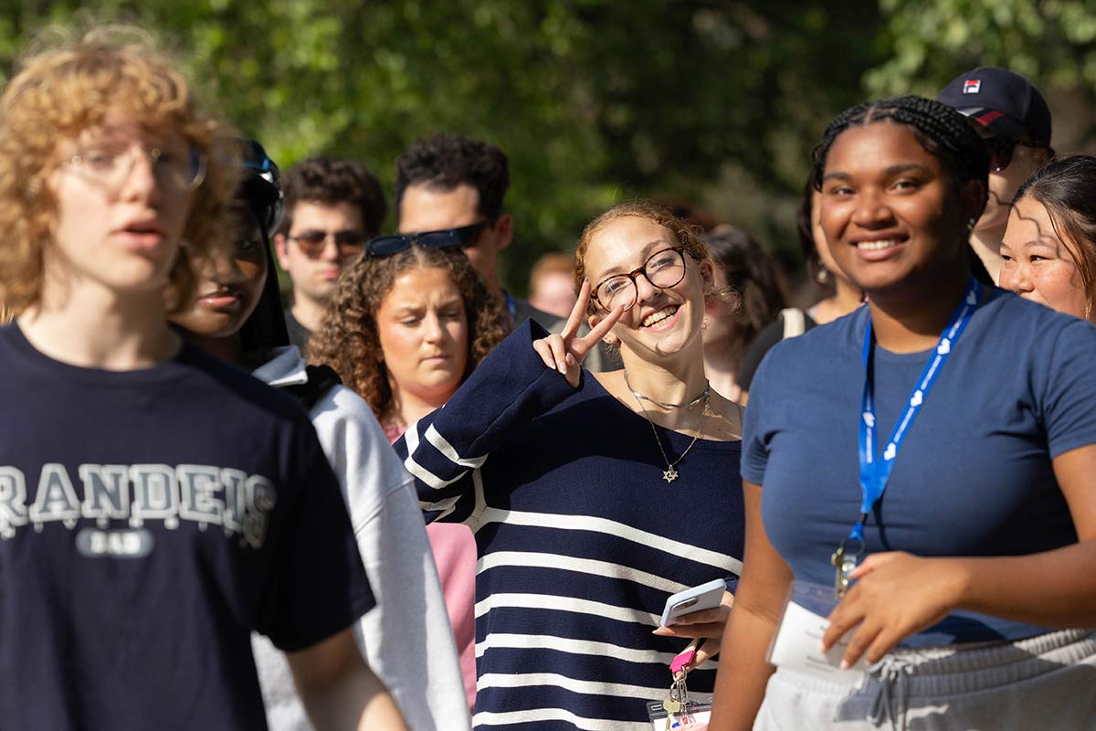 People walking around campus and smiling, one giving a peace sign