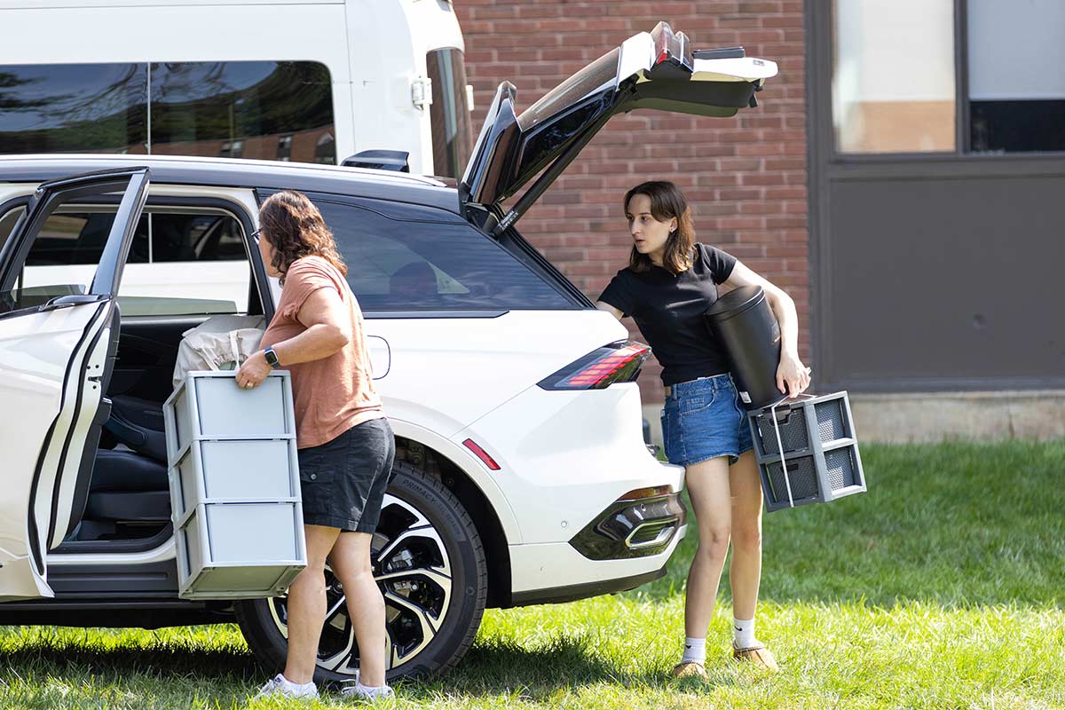 Two people unload items from a car.