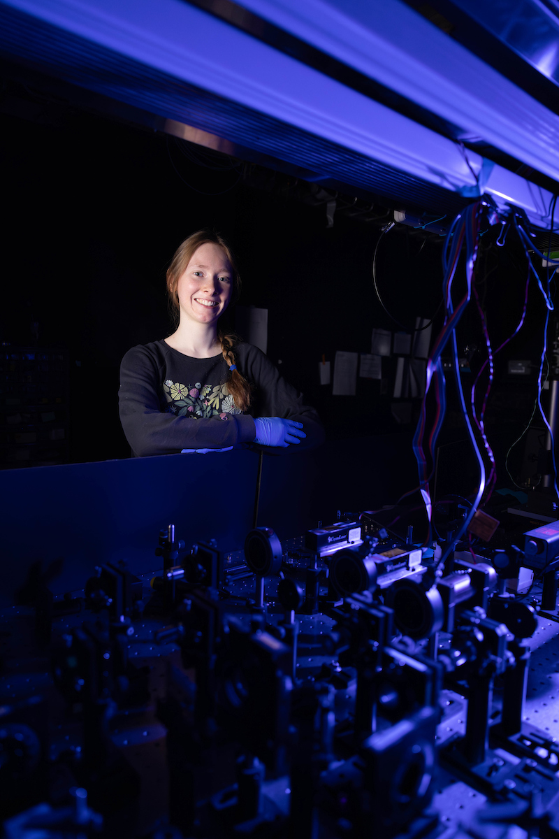 Fiona Stewart stands behind a laser table, a large metal table used to prop up an array of lenses and mirrors.