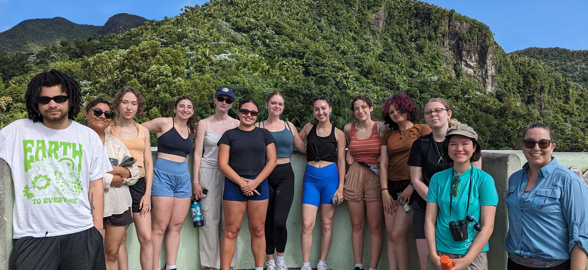 Brandeis students stand in front of a tropical hillside in Puerto Rico.