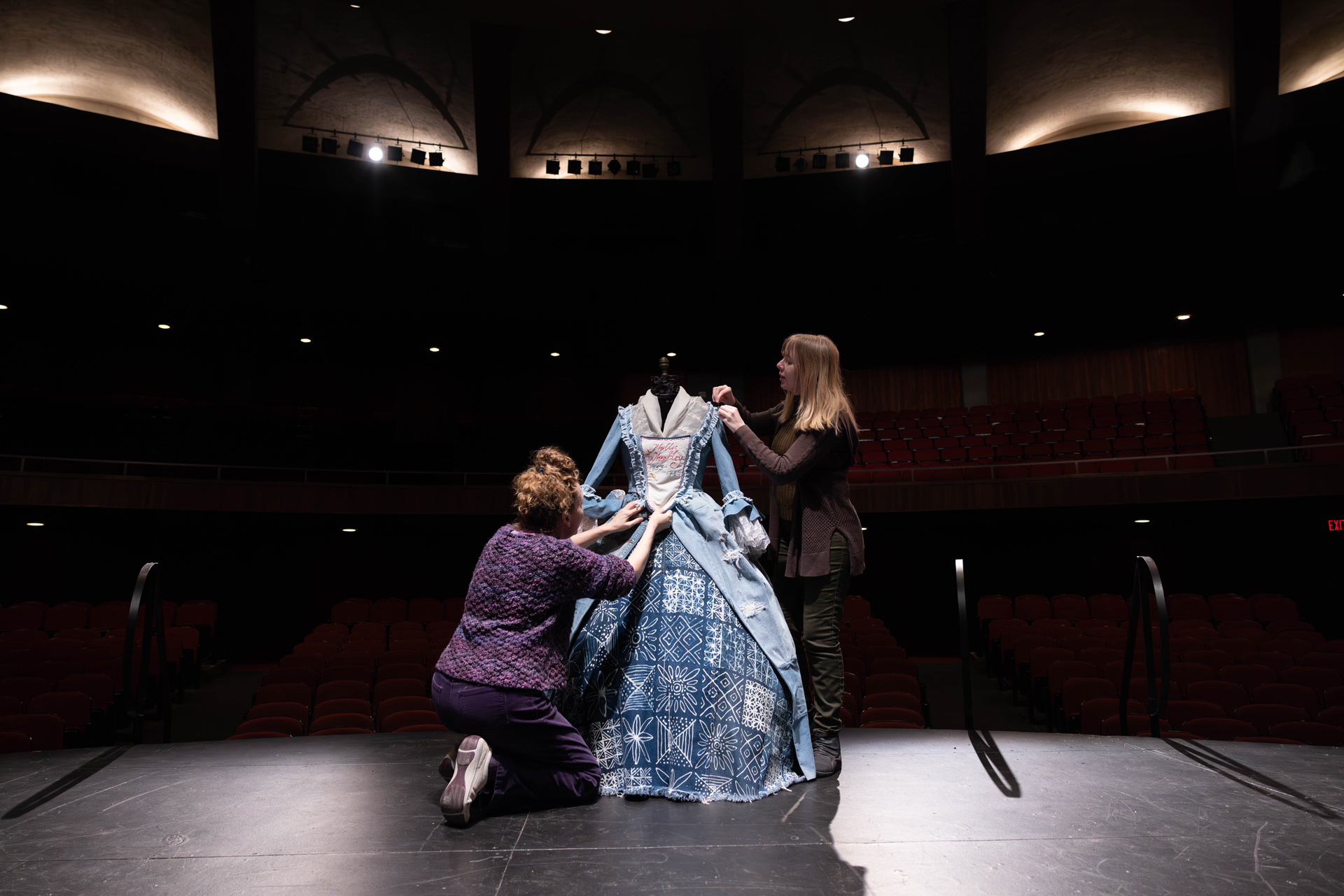 two people make adjustments to a denim dress.