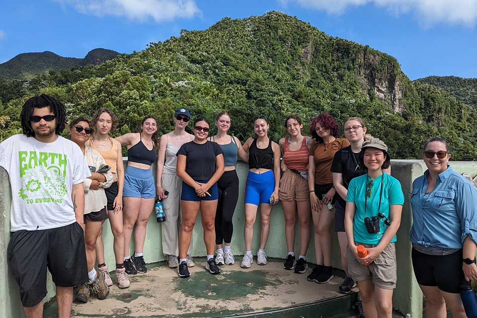 Brandeis students stand in front of a tropical hillside in Puerto Rico.