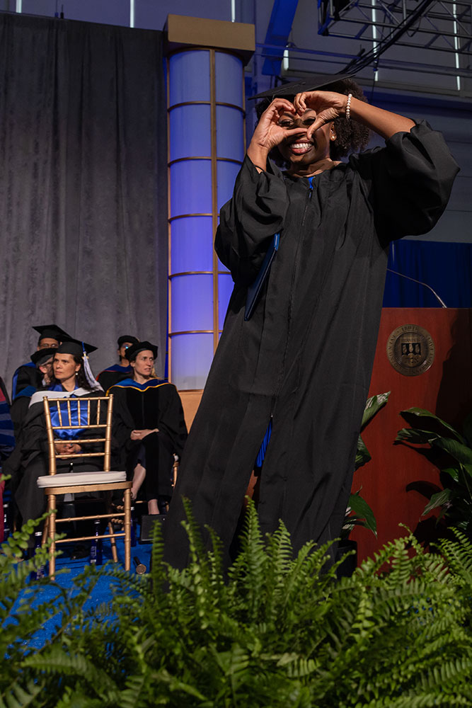 A graduate walking the stage making a heart with their hands