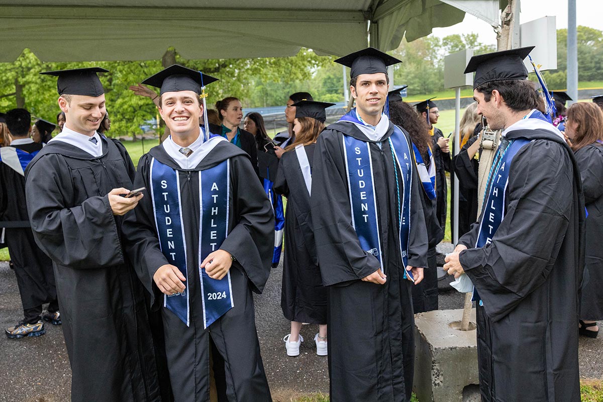 A group of graduates stand outside beneath a white tent.
