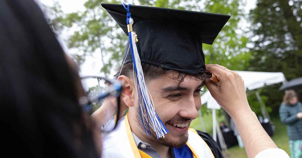 A graduate smiles as someone helps adjust their cap.