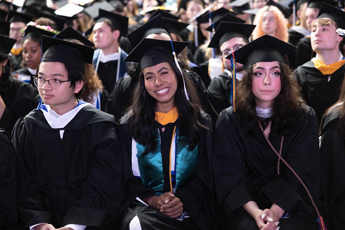 Graduates sit in chairs in Commencement attire at the Commencement ceremony.
