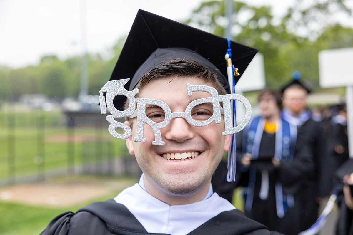 A graduate smiles while wearing funny glasses that spell out the word GRAD.