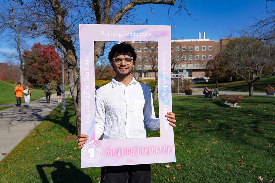 Musa holds a frame around his face with phrases that celebrate being FirstGen