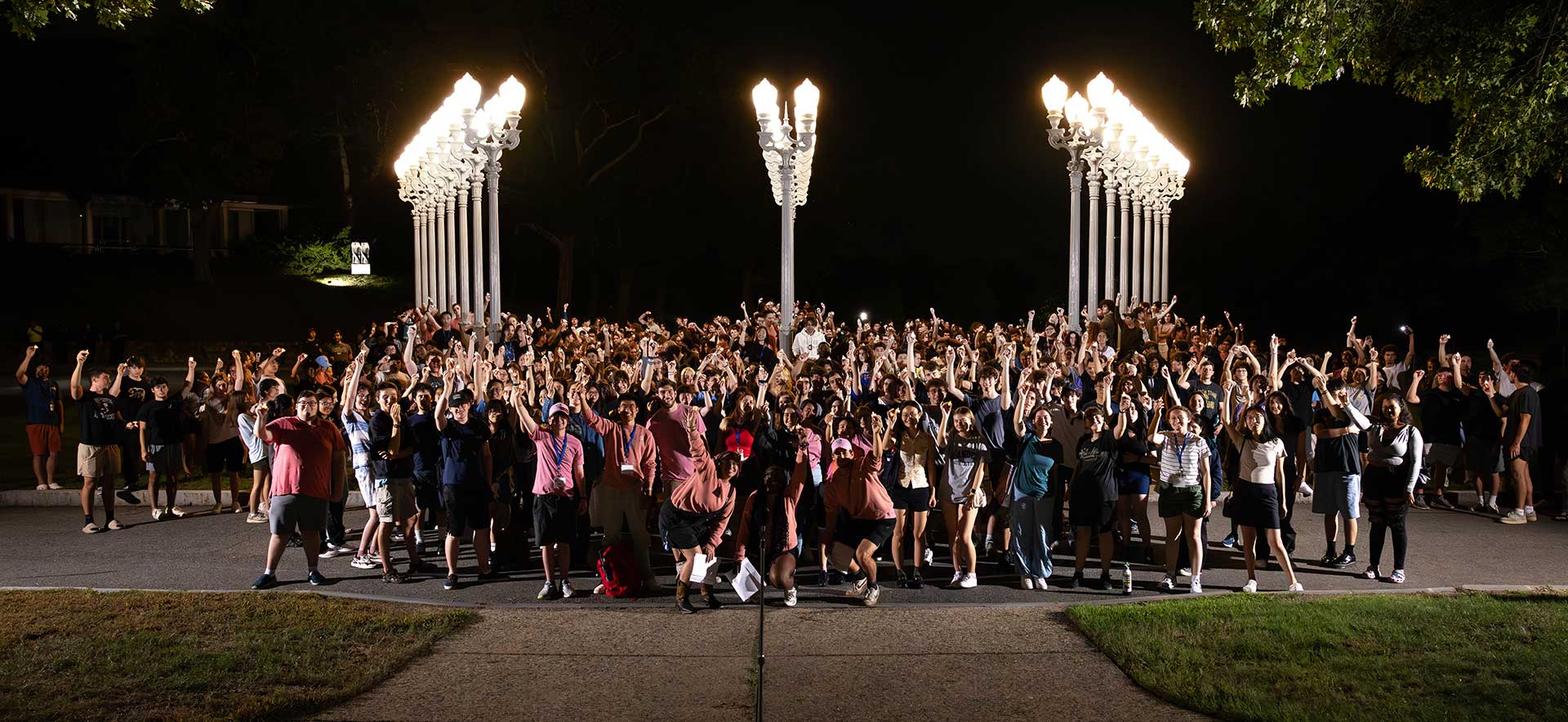 First year students stand holding candles at the Light of Reason statue during the Light the Night orientation event