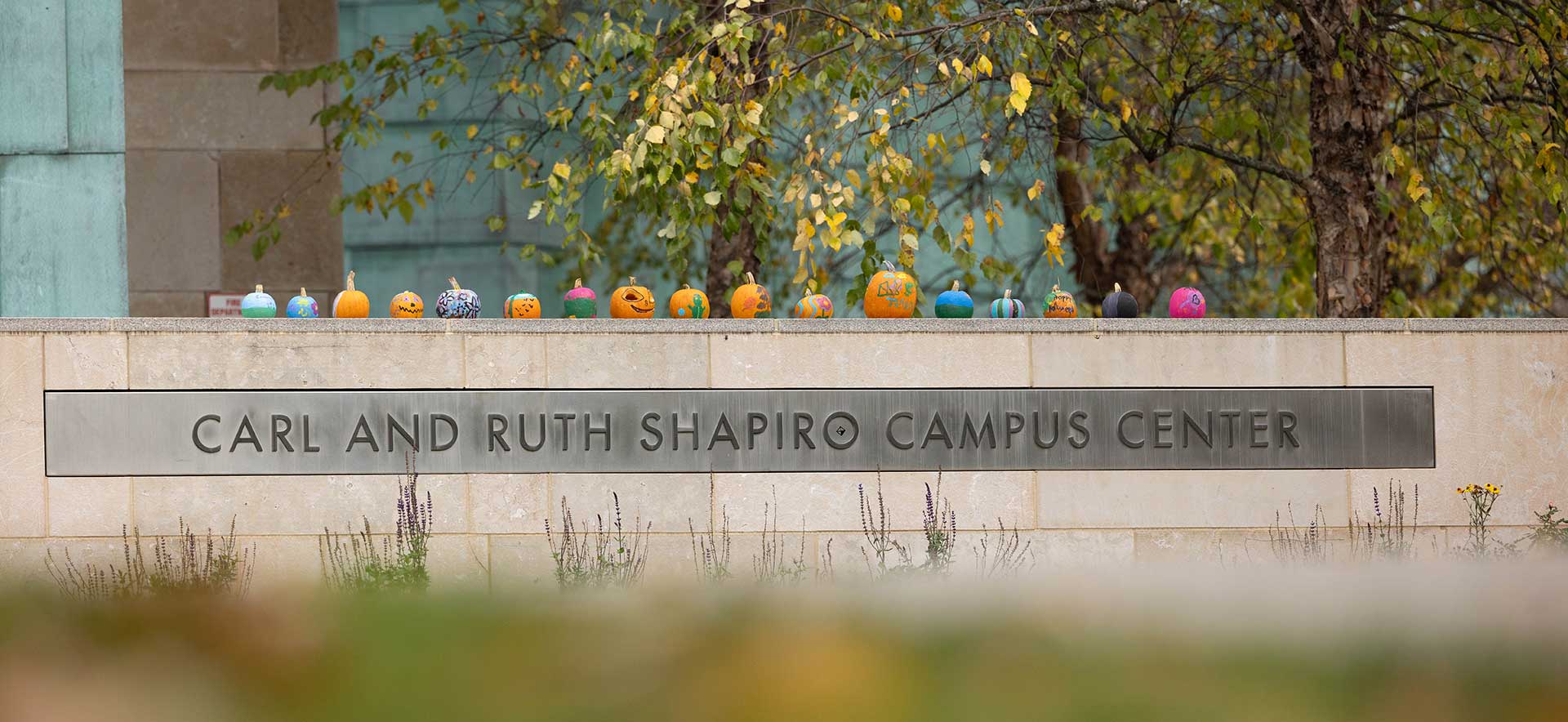 Painted pumpkins line the top of the Carl and Ruth Shapiro Campus Center sign