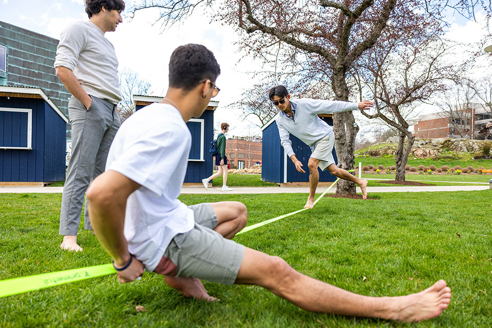Students balance on a slackline outdoors on a spring day.