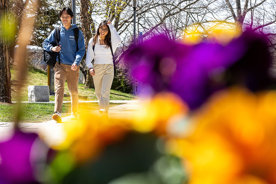 Two students walk through campus on a sunny day.