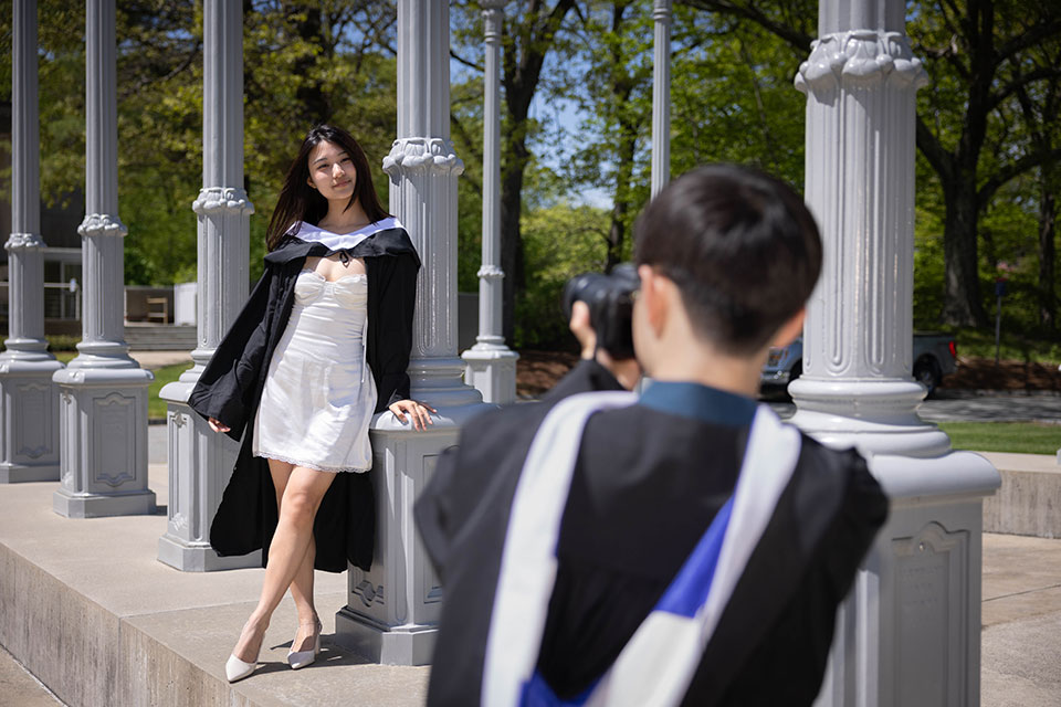 A student take a photo of another graduate dressed in a graduation gown