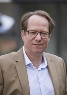 Headshot of Till van Rahden wearing a beige suit jacket and white shirt