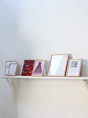 installation view Jaime Black exhibition, monitor on the left side, on the right side is a white shelf with small framed drawings 